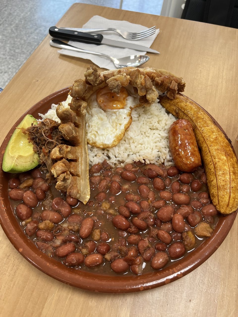 Bandeja Paisa tradicional con frijoles, arroz, chicharrón, huevo frito, chorizo, aguacate y plátano maduro.