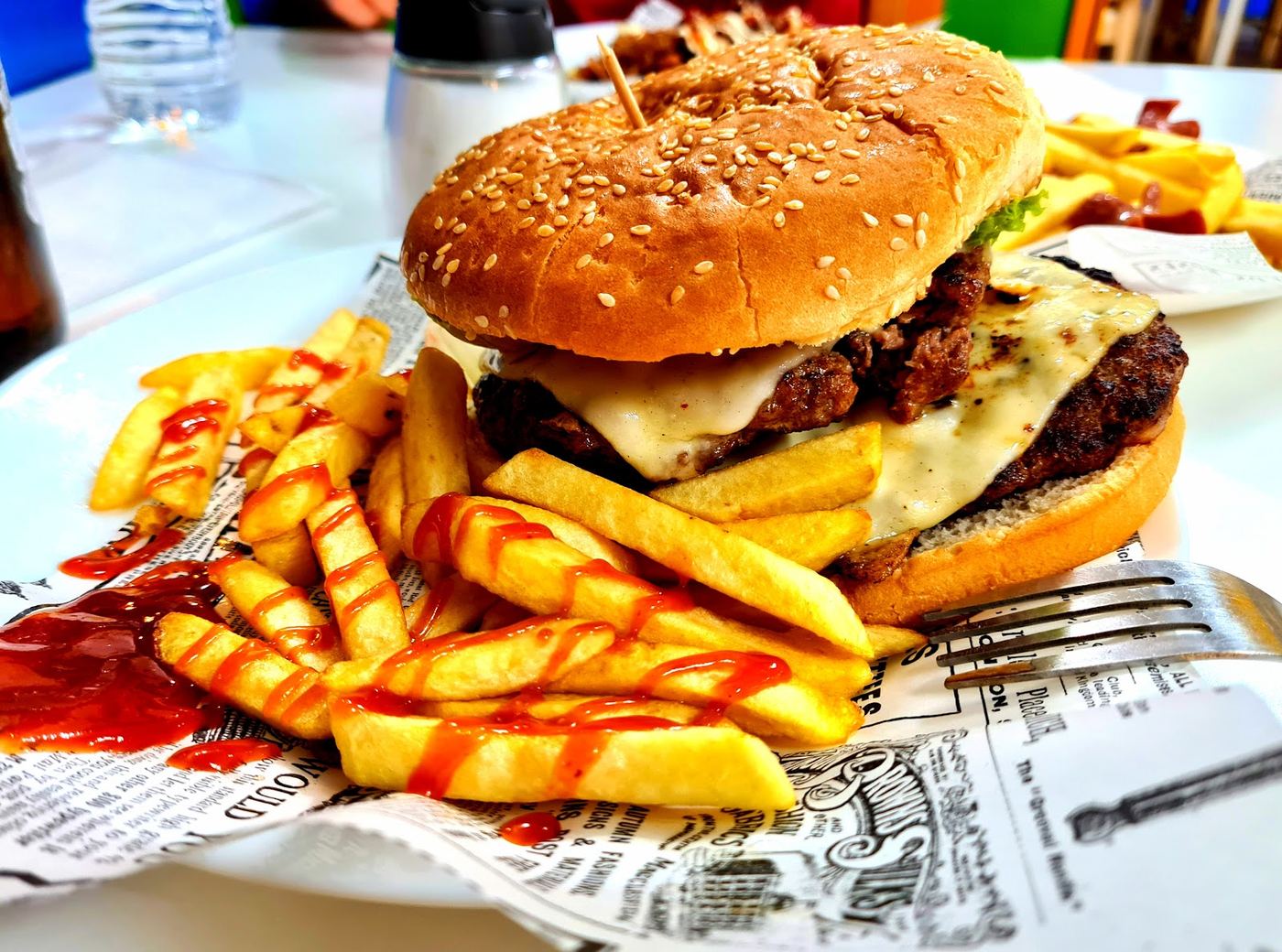 Hamburguesa con queso fundido y patatas fritas, servida en pan de sésamo.